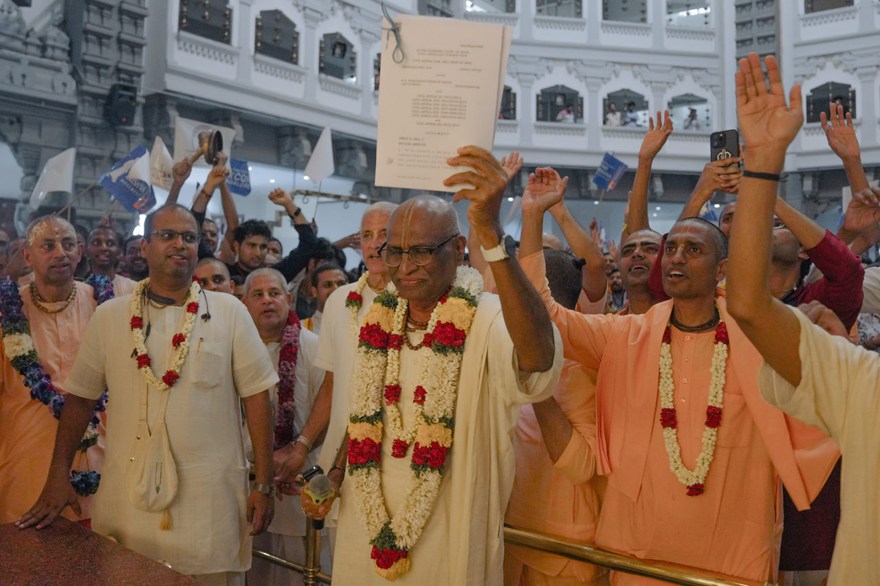 Sri Madhu Pandit Dasa garlanded, surrounded by devotees with flags reading 'Srila Prabhupāda's Glorious Victory'